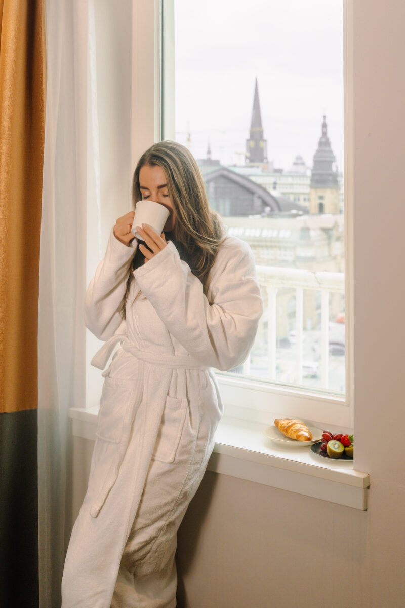 Frau mit Kaffeetasse am Fenster im Hotelzimmer / Woman with a coffee cup at the window in the hotel room