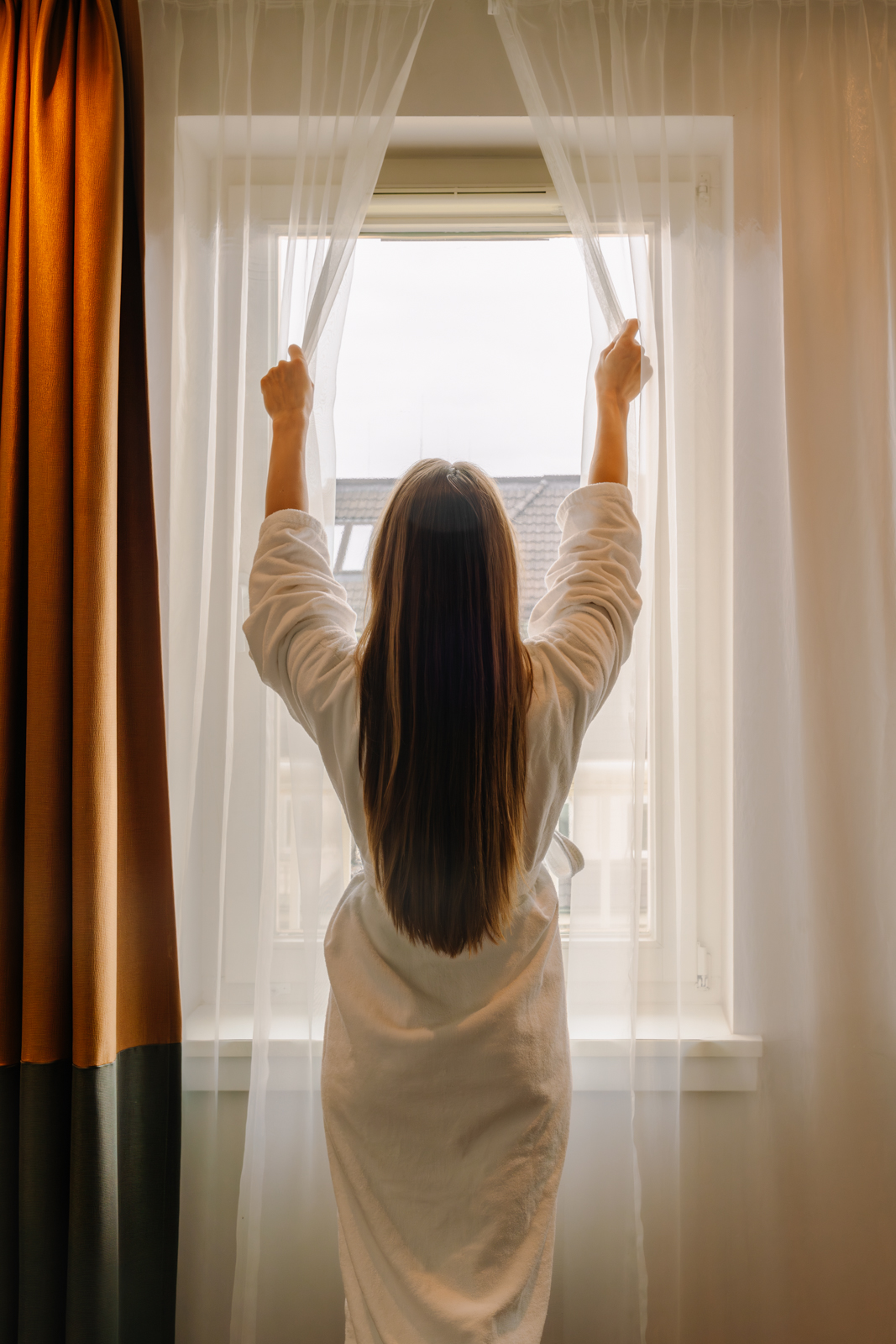 Frau öffnet Vorhang im Hotelzimmer